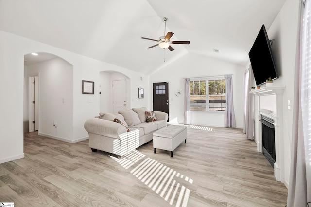 living room featuring high vaulted ceiling, arched walkways, a fireplace, light wood finished floors, and ceiling fan