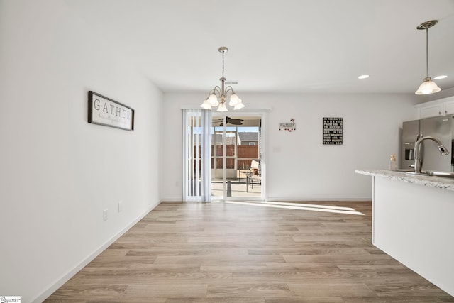 unfurnished dining area with a notable chandelier, baseboards, light wood finished floors, and a sink