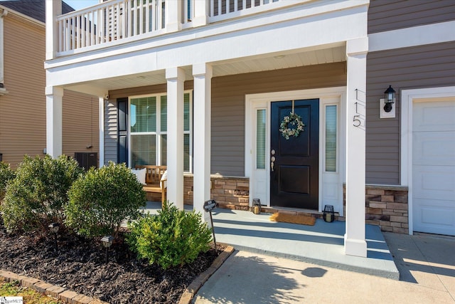 view of exterior entry with a garage, stone siding, a balcony, and covered porch