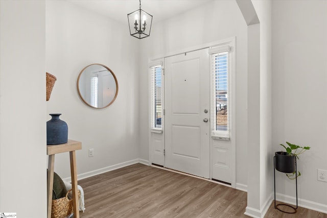 foyer entrance featuring baseboards, arched walkways, an inviting chandelier, and wood finished floors