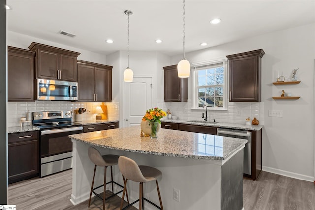 kitchen featuring a kitchen island, dark brown cabinets, stainless steel appliances, and a sink