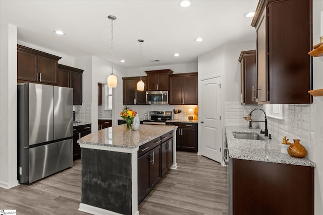 kitchen featuring light wood finished floors, dark brown cabinets, a center island, appliances with stainless steel finishes, and a sink