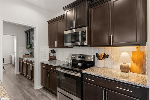 kitchen with light stone countertops, light wood-style flooring, dark brown cabinetry, appliances with stainless steel finishes, and tasteful backsplash