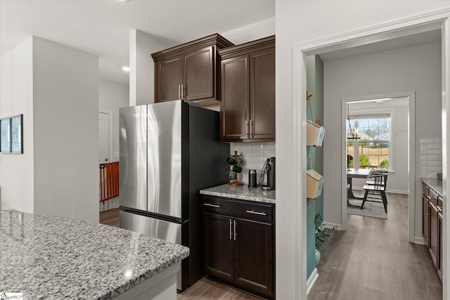 kitchen with light wood finished floors, light stone countertops, dark brown cabinetry, and freestanding refrigerator