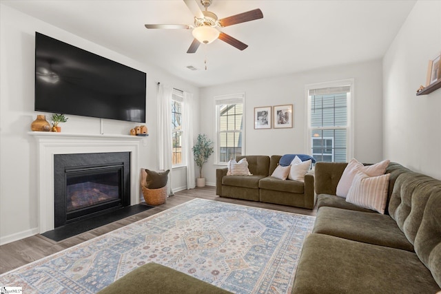 living area with a fireplace with flush hearth, baseboards, a ceiling fan, and wood finished floors