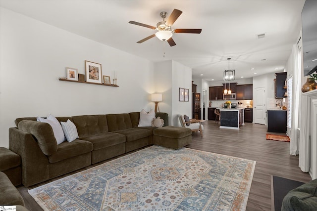 living area with dark wood-style floors, visible vents, ceiling fan with notable chandelier, and recessed lighting