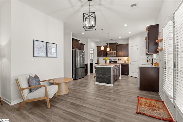 kitchen with wood finished floors, stainless steel appliances, decorative backsplash, dark brown cabinets, and a center island