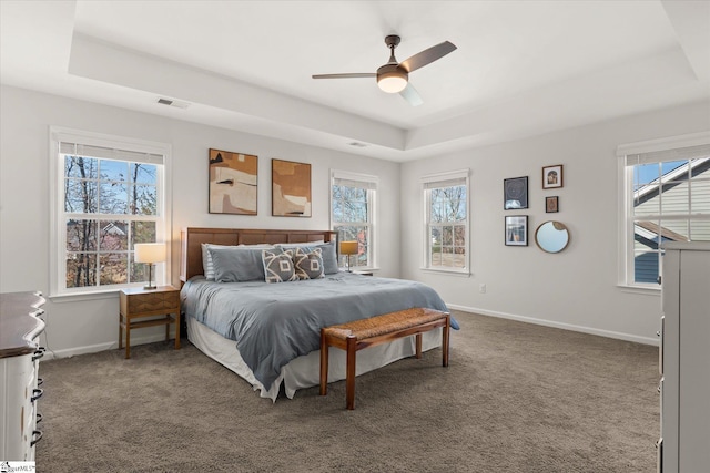 carpeted bedroom with visible vents, a raised ceiling, baseboards, and a ceiling fan