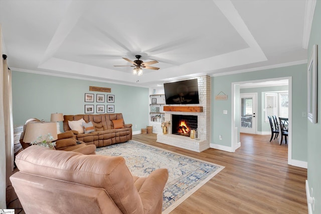 living room featuring baseboards, a tray ceiling, a fireplace, ceiling fan, and light wood-style floors