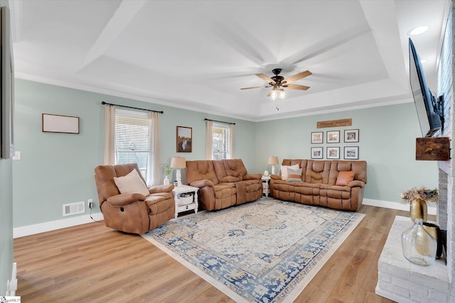 living area featuring visible vents, a raised ceiling, light wood-style floors, and baseboards