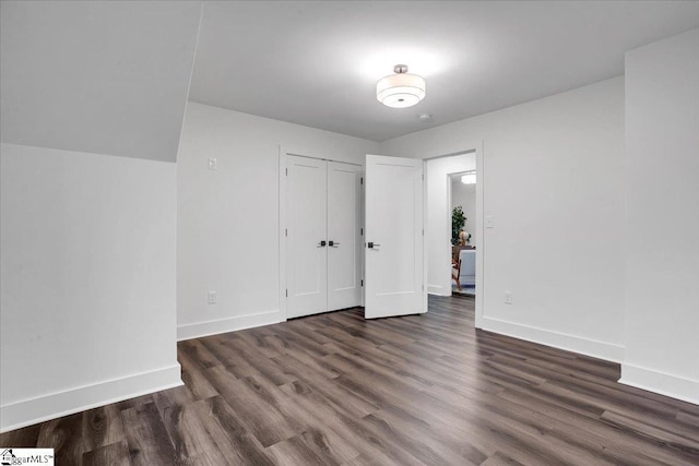 unfurnished bedroom with a closet, baseboards, and dark wood-type flooring