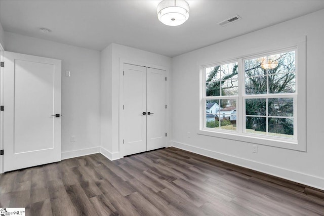 unfurnished bedroom with dark wood finished floors, baseboards, visible vents, and a closet