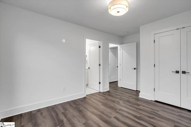 unfurnished bedroom featuring wood finished floors, baseboards, a closet, and connected bathroom