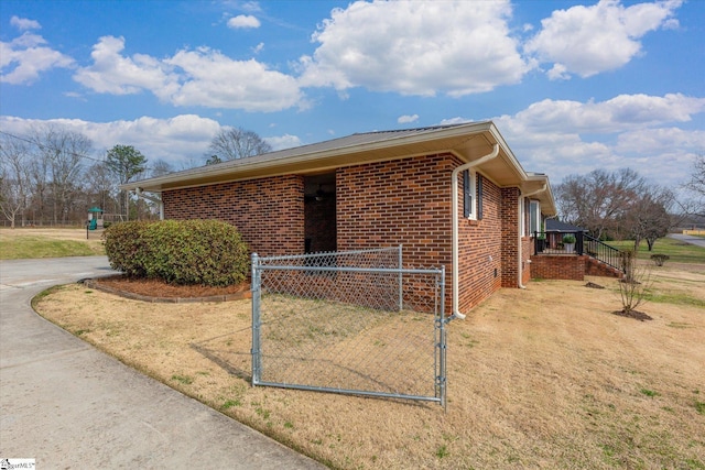 view of side of property featuring concrete driveway, a gate, fence, and brick siding