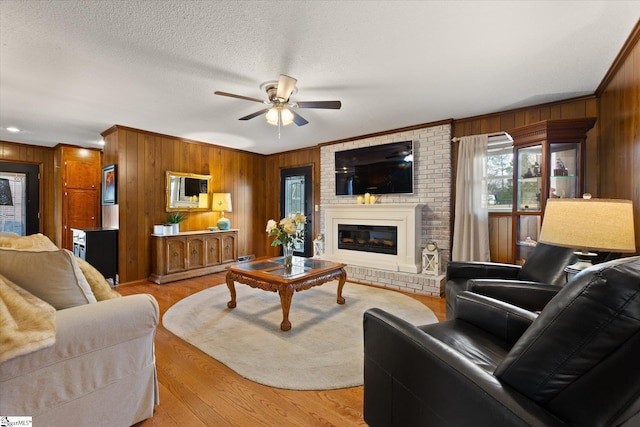 living room featuring light wood-type flooring, a textured ceiling, wooden walls, a fireplace, and ceiling fan