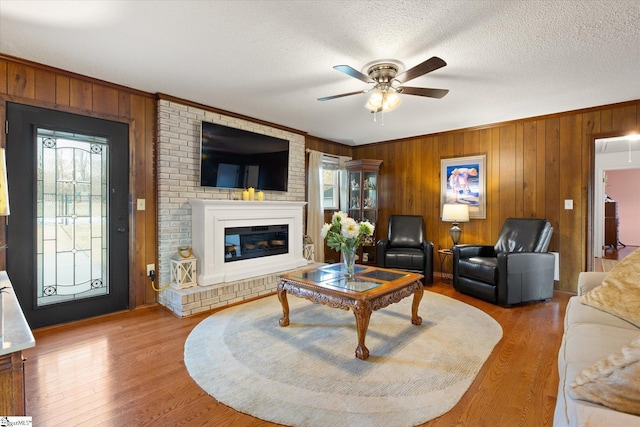 living area featuring ceiling fan, a textured ceiling, a brick fireplace, and wood finished floors