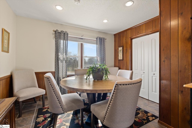 dining area featuring a wainscoted wall, recessed lighting, wood walls, a textured ceiling, and dark tile patterned floors