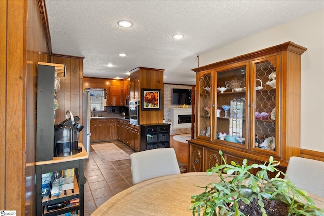 kitchen featuring brown cabinetry, a fireplace, a sink, a textured ceiling, and stainless steel oven