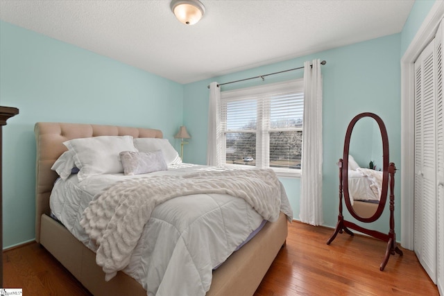 bedroom featuring baseboards, wood finished floors, a closet, and a textured ceiling