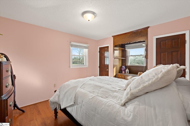 bedroom with multiple windows, a textured ceiling, and wood finished floors