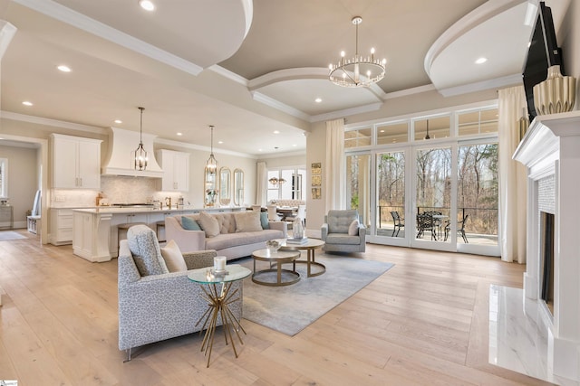 living room featuring a chandelier, a fireplace, light wood-type flooring, and crown molding