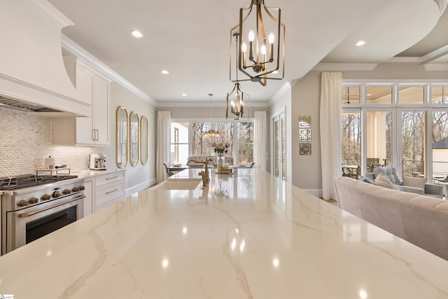 kitchen with an inviting chandelier, custom exhaust hood, stainless steel range, white cabinets, and open floor plan