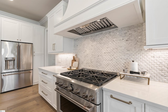 kitchen with high end appliances, premium range hood, light wood-style flooring, white cabinets, and backsplash