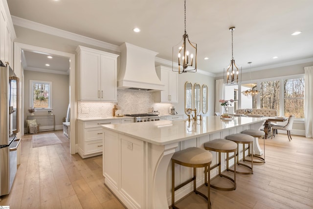 kitchen with premium range hood, light wood-style floors, an inviting chandelier, stove, and stainless steel fridge