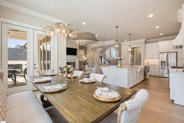 dining area featuring a chandelier, ornamental molding, recessed lighting, a fireplace, and light wood-style floors