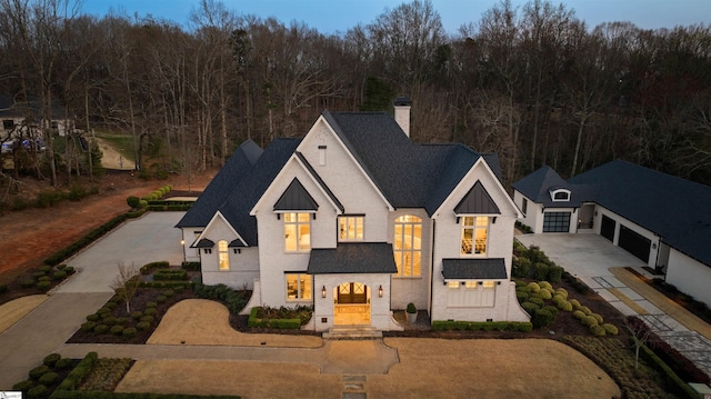 view of front of house with a standing seam roof, a shingled roof, a chimney, concrete driveway, and board and batten siding