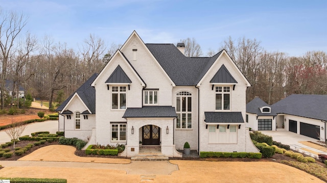 french provincial home featuring driveway, roof with shingles, a standing seam roof, a garage, and brick siding