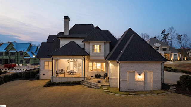 back of property featuring brick siding, a chimney, a patio, and roof with shingles