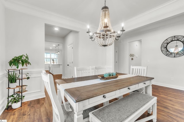 dining area with dark wood finished floors, wainscoting, an inviting chandelier, and ornamental molding