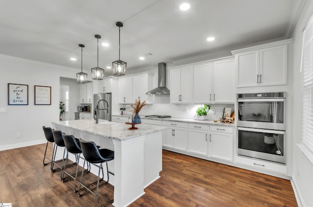 kitchen featuring backsplash, wall chimney range hood, a breakfast bar area, appliances with stainless steel finishes, and white cabinets