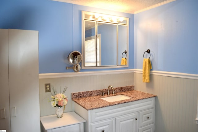 bathroom featuring wainscoting, crown molding, a textured ceiling, and vanity