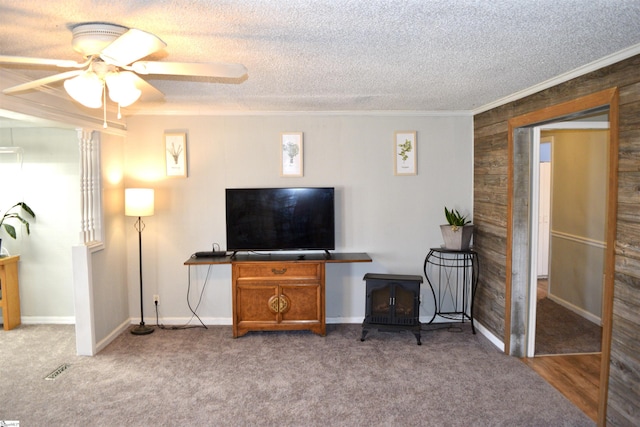 carpeted living area featuring crown molding, baseboards, ceiling fan, a wood stove, and a textured ceiling