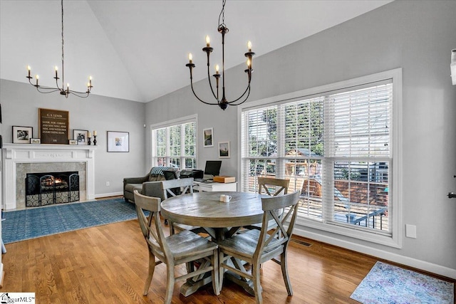 dining area with baseboards, wood finished floors, a chandelier, and a tiled fireplace