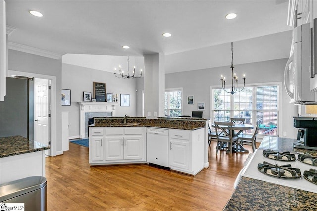 kitchen featuring white appliances, a fireplace, a sink, white cabinetry, and a chandelier