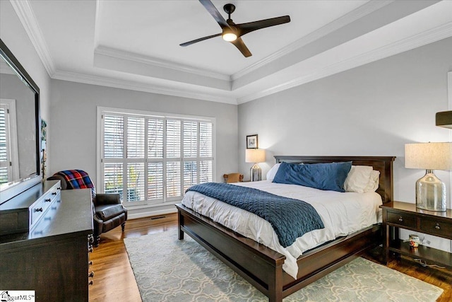 bedroom featuring wood finished floors, visible vents, ceiling fan, ornamental molding, and a raised ceiling