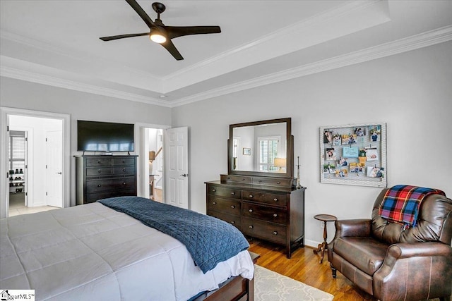 bedroom featuring a ceiling fan, wood finished floors, baseboards, a tray ceiling, and crown molding