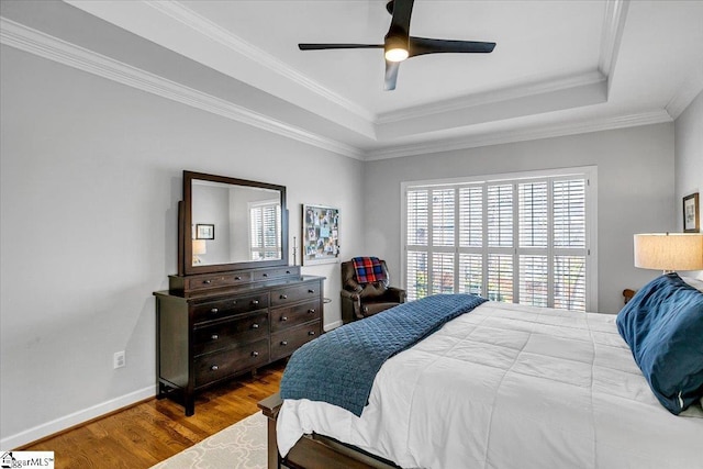 bedroom featuring a raised ceiling, wood finished floors, crown molding, baseboards, and ceiling fan