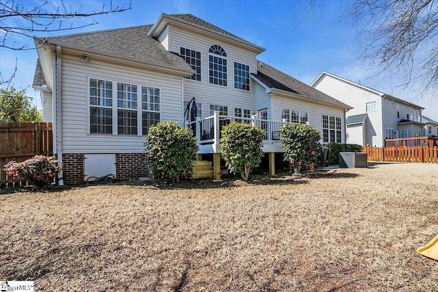 back of property with a shingled roof, a deck, and fence