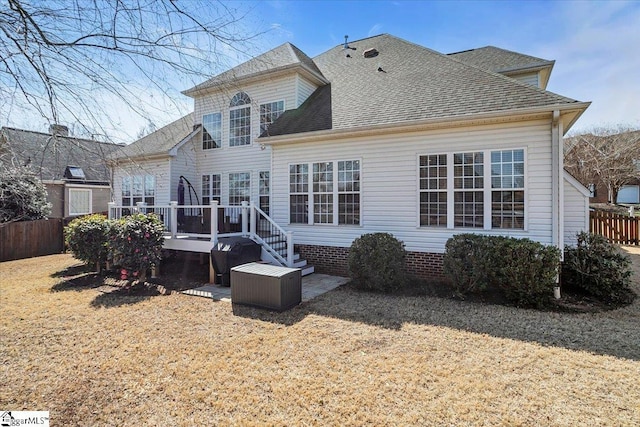 back of property featuring a lawn, roof with shingles, a deck, and fence