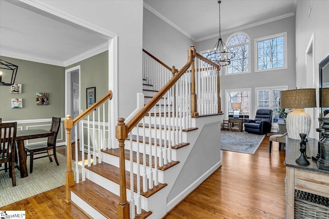 stairs with a high ceiling, a notable chandelier, wood finished floors, and ornamental molding