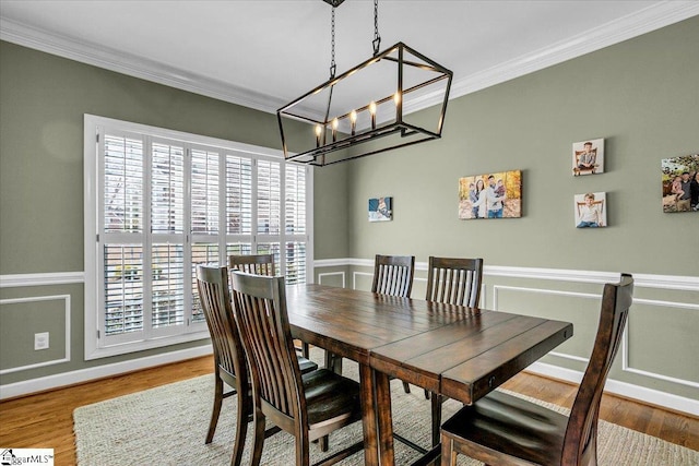 dining area with a wainscoted wall, a notable chandelier, wood finished floors, and crown molding