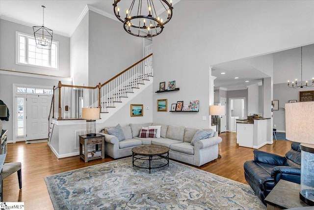 living room with ornamental molding, wood finished floors, a towering ceiling, stairway, and a chandelier