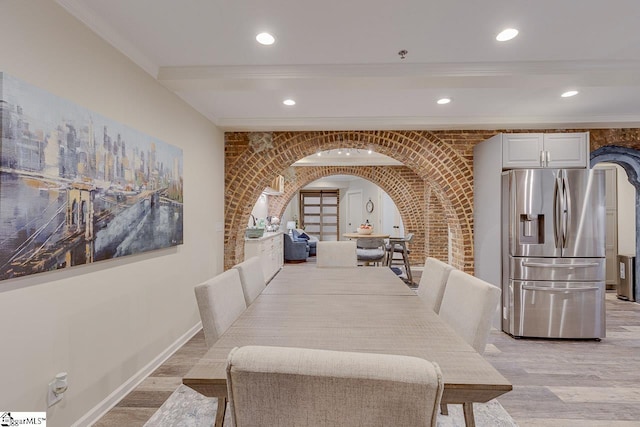 dining space featuring arched walkways, light wood-style flooring, brick wall, and baseboards