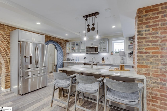 kitchen with tasteful backsplash, stainless steel appliances, a breakfast bar area, glass insert cabinets, and light stone countertops