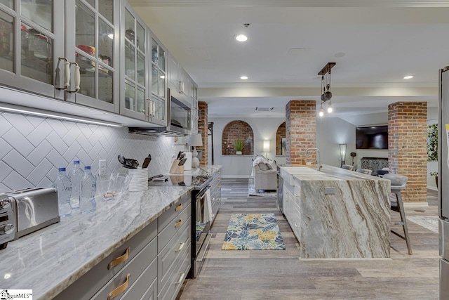 kitchen with stainless steel microwave, open floor plan, electric range oven, ornamental molding, and light stone counters