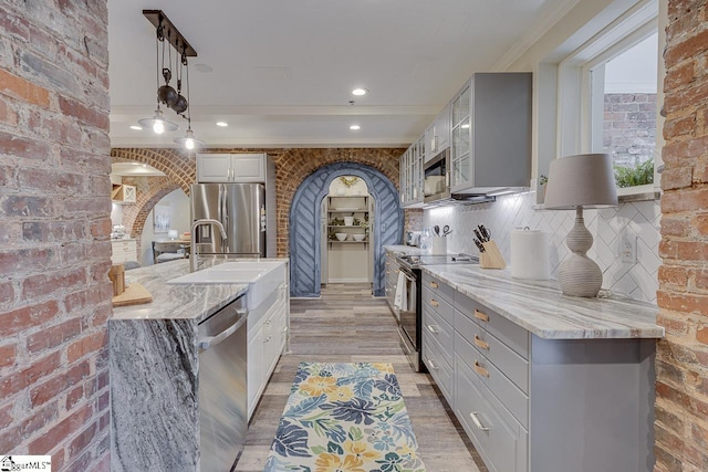 kitchen featuring brick wall, arched walkways, appliances with stainless steel finishes, and a sink